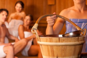 Close up of sauna bucket in hand of sauna user in front of other sauna users