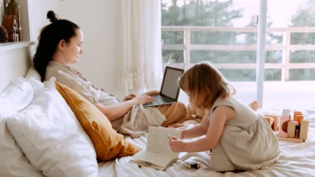 Woman on Laptop sitting on bed with daughter